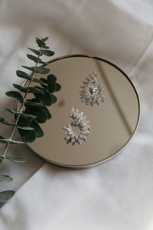 diamond earrings laying on a small mirror beside a eucalyptus branch