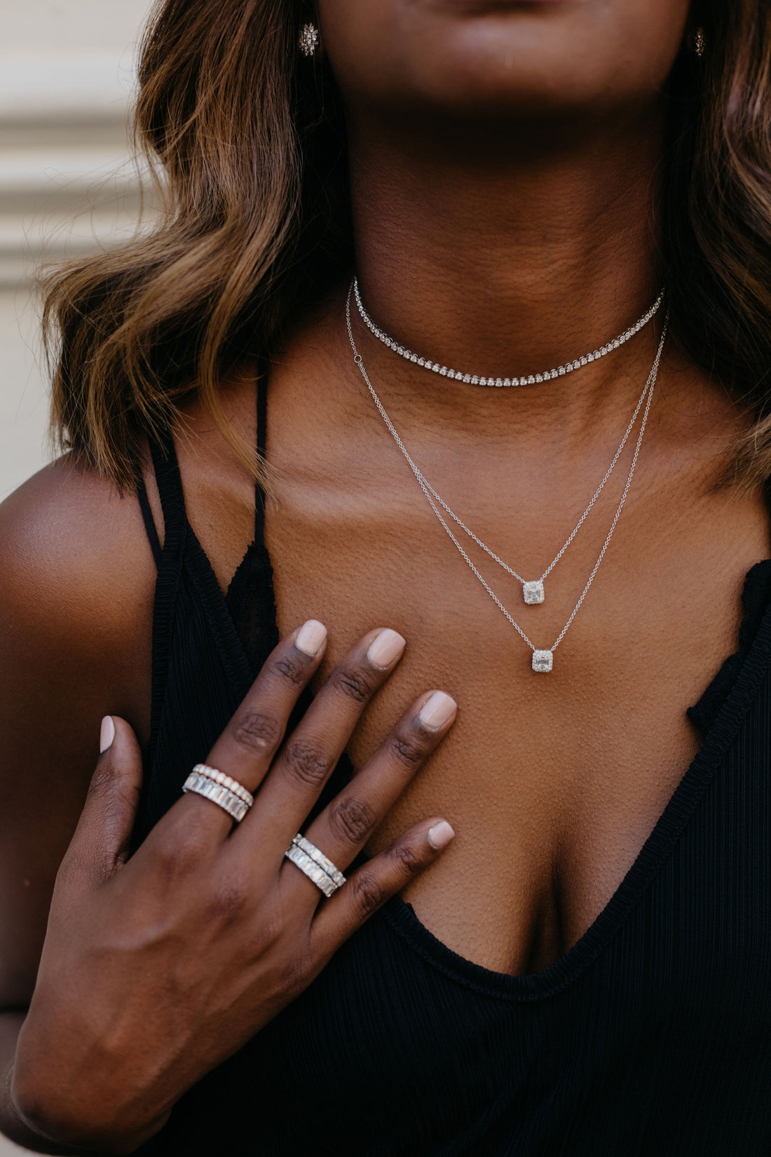 woman in tank top showing off diamond rings and layered diamond necklaces